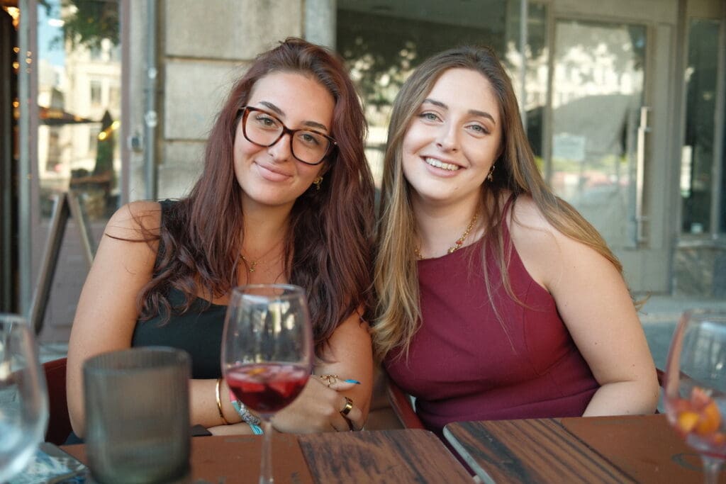 Two friends smiling at an outdoor restaurant in Porto, Portugal, enjoying drinks and good conversation while exploring the city together.