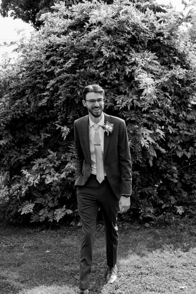 Black and white portrait of the groom standing among the vineyard greenery at Waupoos Estates Winery.