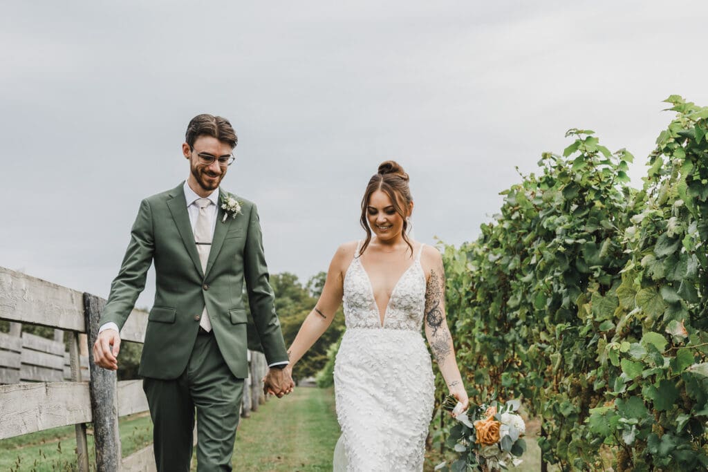 Bride and groom holding hands and walking through the vineyard together after their wedding ceremony.
