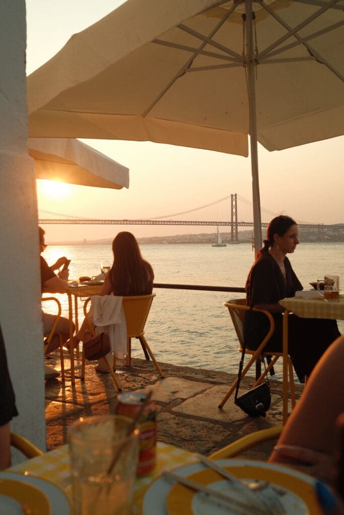 People enjoying dinner by the water as the sun sets over Porto, Portugal.