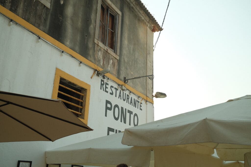 Outdoor dining at Ponto Final, a famous riverside restaurant in Almada, Portugal, overlooking the Tagus River and Lisbon at sunset.
