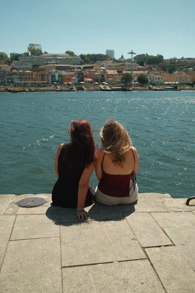 Two friends enjoying the waterfront in Porto, Portugal, overlooking the Douro River and the colorful riverside buildings of the historic Ribeira district.