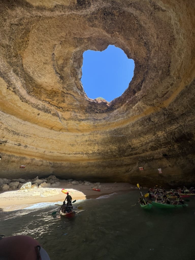Interior view of the famous Benagil Cave in Portugal's Algarve region, with kayakers exploring the sea cave beneath its natural skylight opening.