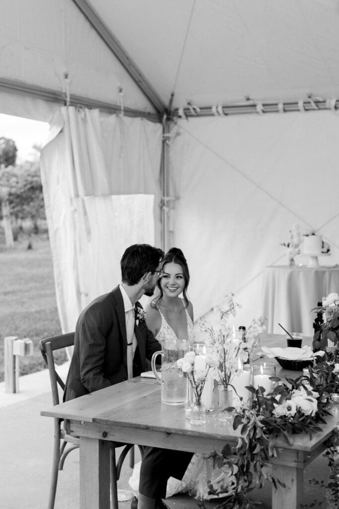 Bride and groom seated together during their wedding reception inside the reception tent at Waupoos Estates Winery.