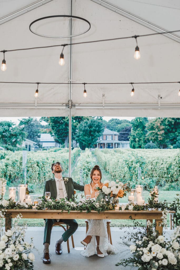 Bride and groom seated at their sweetheart table overlooking the vineyard during their wedding reception.