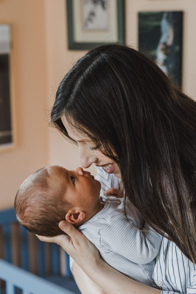 Mother holding her newborn baby close and smiling down at them during a cozy lifestyle newborn session at home.