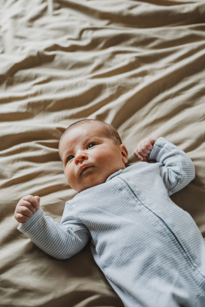Newborn baby lying on a bed wrapped in a soft sleeper during a cozy lifestyle newborn session at home.