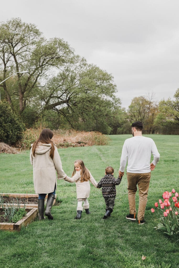 The Turner family walking hand in hand across their backyard, with their newborn baby and two young children enjoying a spring morning together.