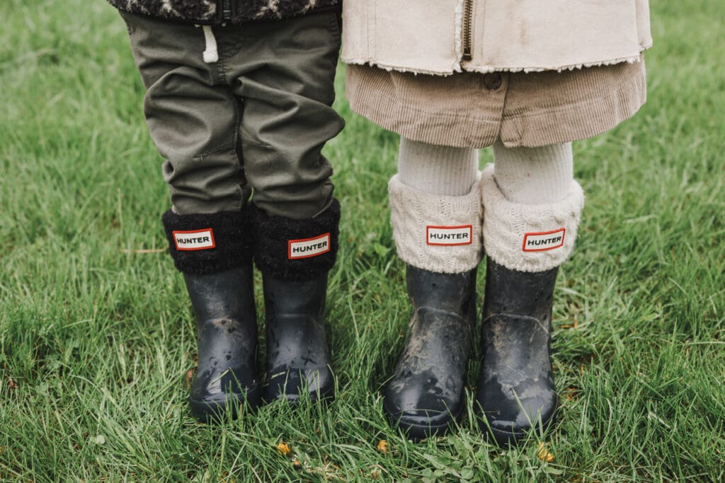 Close-up of two children standing side by side in matching Hunter rain boots during a cozy outdoor newborn and family session.