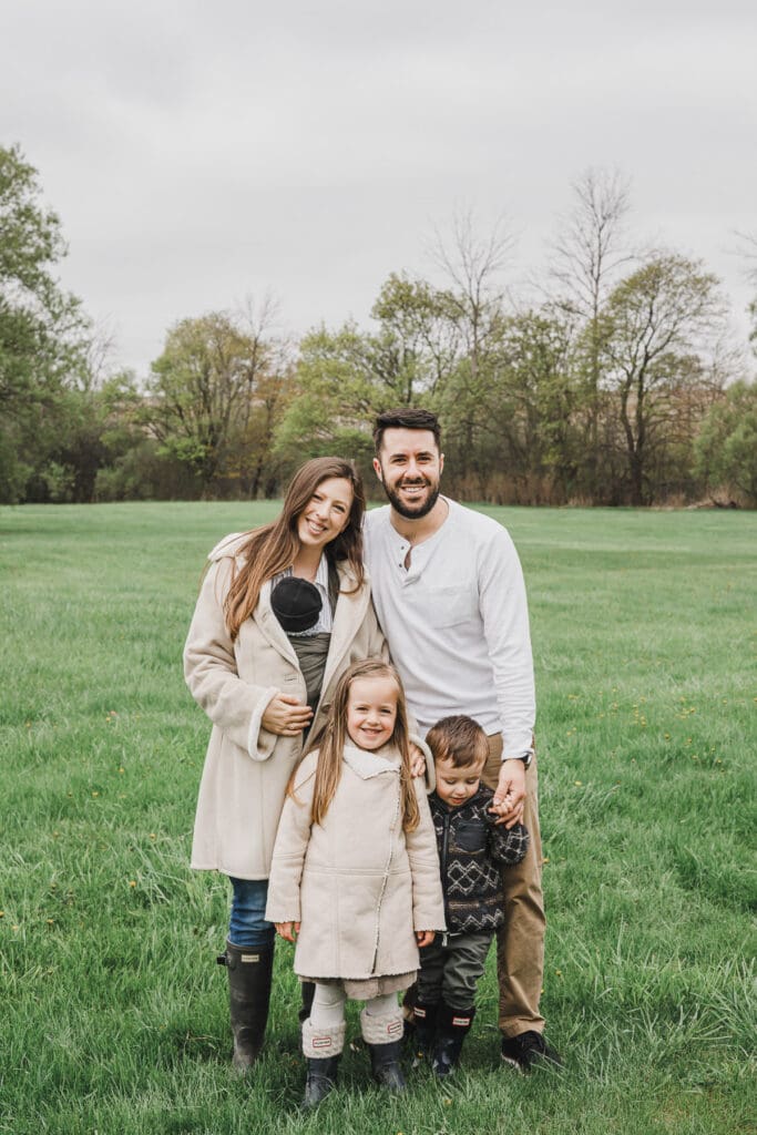 The Turner family gathered together outdoors with their newborn baby and two children, smiling during a relaxed family portrait.